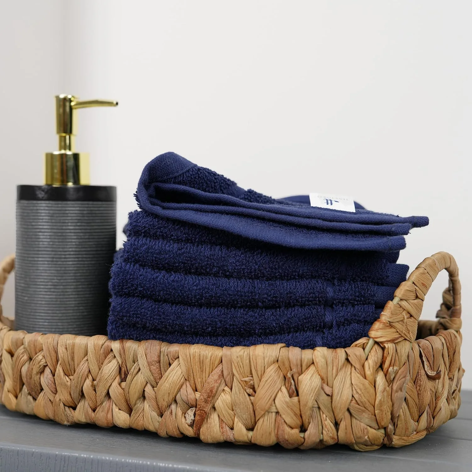 Navy hand towels rolled into a basket beside a soap pump